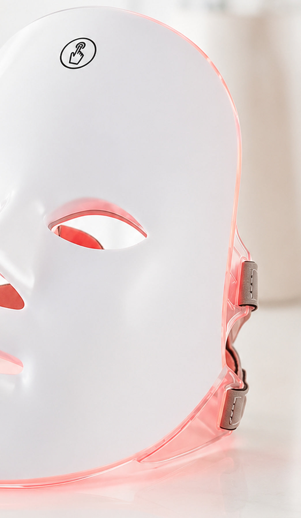Máscara LED facial VELOURA encendida en luz roja sobre lino en una habitación en penumbra